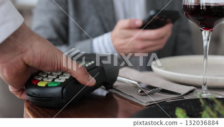 Close up man paying restaurant bill using credit card. Couple spending date in restaurant. Waiter giving terminal wifi scan using smartphone contactless NFC payment. Close up man paying restaurant bill using credit card. Couple spending date in restaurant. Waiter giving terminal wifi scan using smartphone contactless NFC payment. 132036884