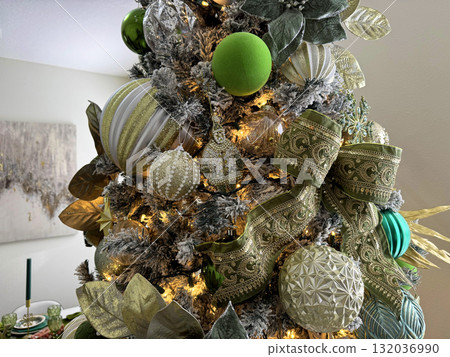 A detailed view of a Christmas tree with elegant ornaments, leaves, and a large green ribbon bow. The gold and silver decorations shine under warm holiday lights. 132036990