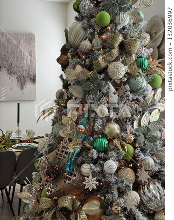 A close-up of a Christmas tree beautifully decorated in green, gold, and silver ornaments. The festive design includes ribbons, lights, and an elf figure for charm. 132036997