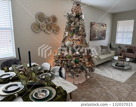 A cozy living room glows with a beautifully decorated Christmas tree and festive dining table. Warm light and soft tones create an elegant holiday atmosphere. 132037015