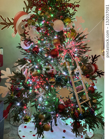 A close-up view shows colorful ornaments and glowing lights on a Christmas tree. Red, gold, and green decorations sparkle in a cozy festive interior. A close-up view shows colorful ornaments and glowing lights on a Christmas tree. Red, gold, and green decorations sparkle in a cozy festive interior. 132037081