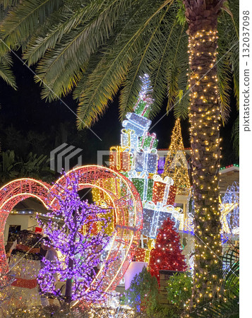 A glowing tower of Christmas presents surrounded by palm trees lights up the tropical night. The colorful festive scene celebrates joy and holiday cheer. A glowing tower of Christmas presents surrounded by palm trees lights up the tropical night. The colorful festive scene celebrates joy and holiday cheer. 132037098