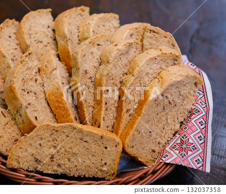 Homemade baking. Close up of sliced rye bread on dark wooden background. Freshly baked fragrant brown bread lies on wooden table on background of ears of rye or wheat. Selective focus. 132037358