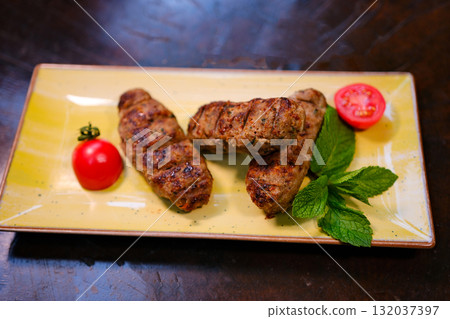 Close-up photo of mixed grilled meat platter. Beef, pork, poultry, sausages, grilled garlic, chili pepper, red tomatoes on wooden rustic background. Close-up photo of mixed grilled meat platter. Beef, pork, poultry, sausages, grilled garlic, chili pepper, red tomatoes on wooden rustic background. 132037397