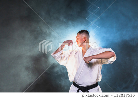 Strong man fighter in white kimono for karate martial arts with black belt preparing for fight training in black background. Man training moves punches kicks practicing shadow fight ready for sparring 132037530
