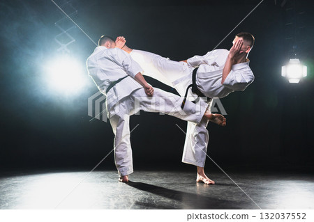 Martial arts masters on dark background. Strong man fighters in white kimono for karate martial arts fighting training in black gym. Karate fighters training punches kicks practicing fight sparring 132037552