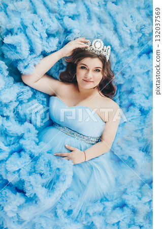 pregnant girl lies on a blue background. girl in a blue dress. girl with a diamond crown. High quality photo 132037569