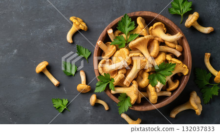 Fresh chanterelle mushrooms in wooden bowl with parsley leaves on dark background. Top view of seasonal edible fungi. Natural organic food ingredient. Fresh chanterelle mushrooms in wooden bowl with parsley leaves on dark background. Top view of seasonal edible fungi. Natural organic food ingredient. 132037833