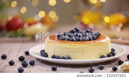 Cheesecake topped with fresh blueberries on white plate, festive bokeh background, delicious homemade dessert for celebration 132037852