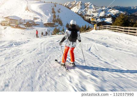 Young adult confident woman skier skiing fast downhill winter alpine skiing resort. Female sporty person with backpack mountain Alps snow slope outdoors cold snowy sunny backlit light day 132037990