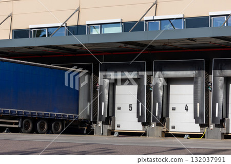 Innovative modern logistics warehouse center complex building exterior bay gate semi-trailer unloading goods distribution warm blue sunset sky background. Cargo storage facility industry building Innovative modern logistics warehouse center complex building exterior bay gate semi-trailer unloading goods distribution warm blue sunset sky background. Cargo storage facility industry building 132037991