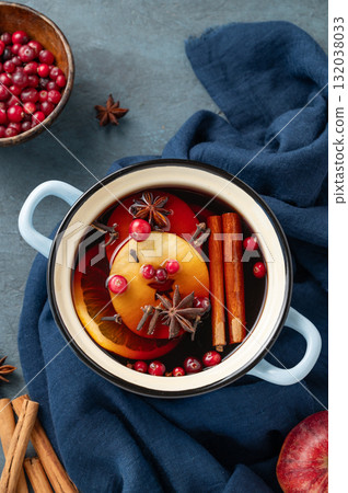 A pot of red mulled wine with spices, orange, apple slices and cranberries on a dark blue background 132038033