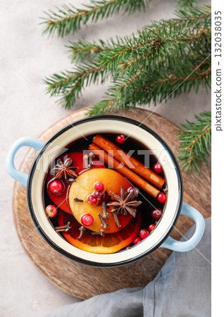 A pot of red mulled wine with spices, orange, apple slices, and cranberries on a wooden board A pot of red mulled wine with spices, orange, apple slices, and cranberries on a wooden board 132038035