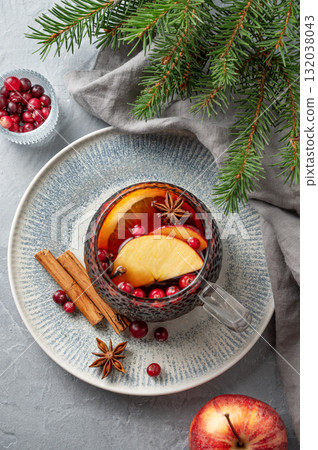 A cup of red mulled wine with spices, orange, apple slices and cranberry  on a gray background 132038043