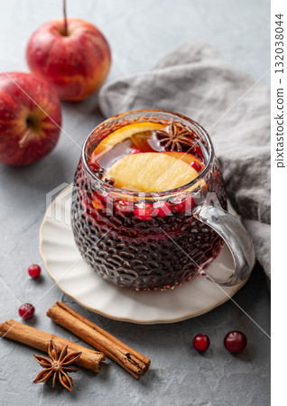 A cup of red mulled wine with spices, orange, apple slices and cranberry on a gray background 132038044
