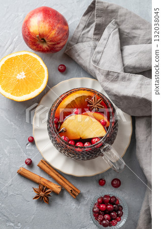 A cup of red mulled wine with spices, orange, apple slices and cranberry on a gray background A cup of red mulled wine with spices, orange, apple slices and cranberry on a gray background 132038045