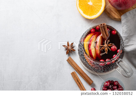 A cup of red mulled wine with spices, orange and apple slices on a light background A cup of red mulled wine with spices, orange and apple slices on a light background 132038052