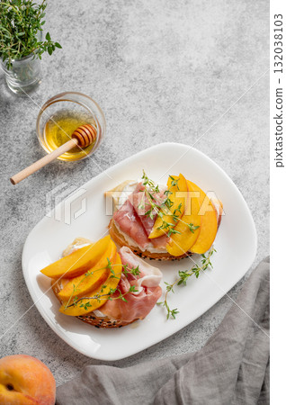 Toast with peach, cream cheese, ham and honey on a plate on a gray background Toast with peach, cream cheese, ham and honey on a plate on a gray background 132038103