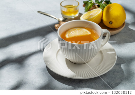 Hot tea with lemon, ginger, honey, and mint in a cup on a blue background with citrus fruits Hot tea with lemon, ginger, honey, and mint in a cup on a blue background with citrus fruits 132038112
