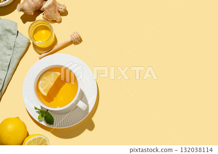 Hot tea with lemon, ginger, honey, and mint in a cup on a yellow background with shadows. 132038114