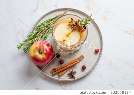 Hot apple cider with cinnamon, anise, and rosemary in glass on a marble background with cranberry 132038124