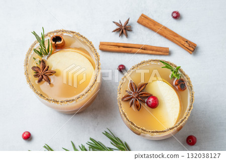 Two glasses of apple cider with cinnamon, anise, brown sugar and rosemary on a light background Two glasses of apple cider with cinnamon, anise, brown sugar and rosemary on a light background 132038127