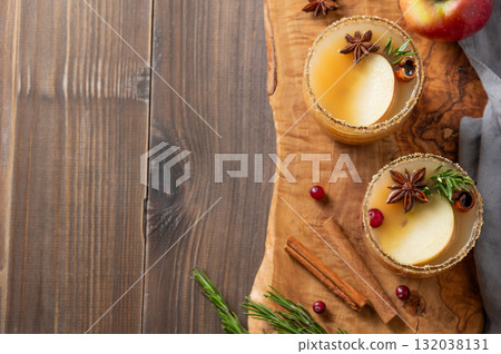 Two glasses of hot apple cider with cinnamon, anise, brown sugar and rosemary on a wooden background 132038131