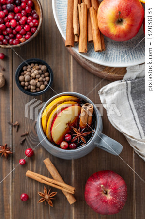 A cup of red mulled wine with spices, orange, apple slices and cranberry on a wooden background 132038135
