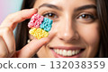 Close-up of a smiling woman holding a colorful piece of porous candy. Selective focus on the unique texture of a sweet snack 132038359