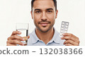 A man holds a blister pack of pills and a glass of water for medical treatment. Close-up portrait of a person taking daily medication. Healthcare and wellness concept on a white background 132038366