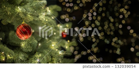 Close-up of a Christmas tree branch with a red ornament and glowing lights against a soft bokeh background, creating a festive and dreamy atmosphere. Close-up of a Christmas tree branch with a red ornament and glowing lights against a soft bokeh background, creating a festive and dreamy atmosphere. 132039054