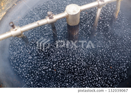 Coffee roasting process in a traditional setup with dark roasted beans in a large roasting machine surrounded by smoke 132039067
