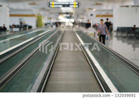 Walkway at a busy airport terminal with travelers moving towards their gates during daytime 132039091