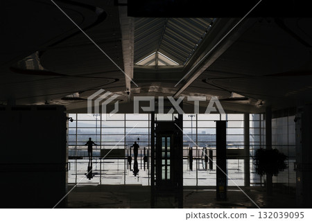 Busy terminal in the late afternoon capturing the silhouettes of travelers against bright windows overlooking the city skyline Busy terminal in the late afternoon capturing the silhouettes of travelers against bright windows overlooking the city skyline 132039095