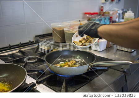 Chef adding marinated chicken to pan in indian restaurant kitchen Chef adding marinated chicken to pan in indian restaurant kitchen 132039823