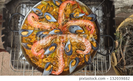 Traditional spanish paella with seafood on outdoor grill for culinary delight. Top view. Typical cuisine of Spain. Valencian cuisine. Stage of cooking paella. Ingredients for paella Traditional spanish paella with seafood on outdoor grill for culinary delight. Top view. Typical cuisine of Spain. Valencian cuisine. Stage of cooking paella. Ingredients for paella 132039882