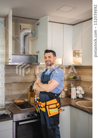 Handyman smiling with crossed arms after installing range hood in kitchen Handyman smiling with crossed arms after installing range hood in kitchen 132039892