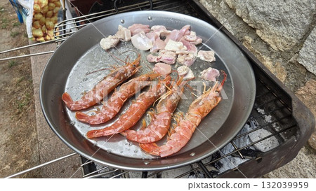Traditional spanish paella preparation with fresh seafood and meat on outdoor grill. Typical cuisine of Spain. Valencian cuisine. Stage of cooking paella. Ingredients for paella Traditional spanish paella preparation with fresh seafood and meat on outdoor grill. Typical cuisine of Spain. Valencian cuisine. Stage of cooking paella. Ingredients for paella 132039959