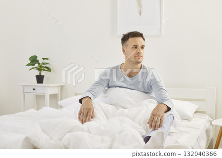 Man in pajamas wakes up in morning with slightly tired expression, probably due to restless sleep. Man in pajamas wakes up in morning with slightly tired expression, probably due to restless sleep. 132040366