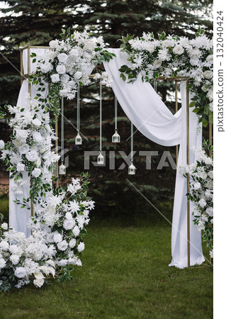 Wedding arch with white flowers and fabric in outdoor garden setting Wedding arch with white flowers and fabric in outdoor garden setting 132040424