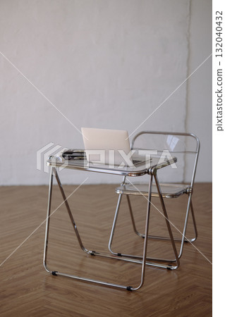 Minimalist chrome desk and transparent chair with laptop on wooden floor against white wall Minimalist chrome desk and transparent chair with laptop on wooden floor against white wall 132040432