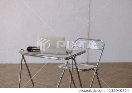 Minimalist chrome desk and transparent chair with laptop on wooden floor against white wall Minimalist chrome desk and transparent chair with laptop on wooden floor against white wall 132040434