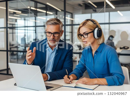 Autistic woman wearing headphone learning with male mentor in real office environment focusing on inclusive professional development and sensory accommodation 132040967