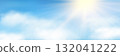 Sun rays, white fluffy clouds on light blue sky background 132041222