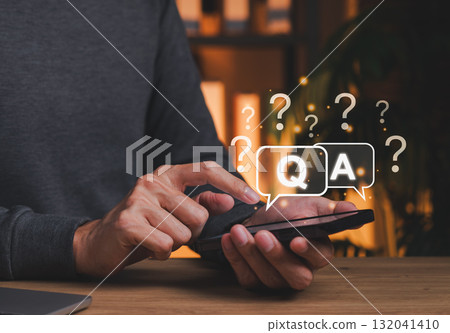 Q&A Chat Interface and Online Support Concept. Person interacts with smartphone speech bubbles marked Q and A surrounded by question marks, symbolizing online help, FAQ systems, digital assistance. Q&A Chat Interface and Online Support Concept. Person interacts with smartphone speech bubbles marked Q and A surrounded by question marks, symbolizing online help, FAQ systems, digital assistance. 132041410