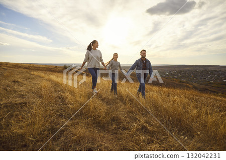 Happy smiling family with child girl walking in the field enjoying nature together. 132042231