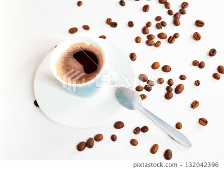 Coffee in a blue cup sits on a white table with coffee beans scattered nearby. 132042396