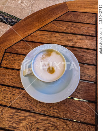 p view of a cappuccino coffee cup with frothy foam and saucer placed on a rustic wooden table. Warm tones and cozy cafe atmosphere. High quality photo p view of a cappuccino coffee cup with frothy foam and saucer placed on a rustic wooden table. Warm tones and cozy cafe atmosphere. High quality photo 132042712