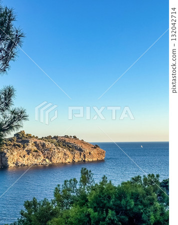 Scenic landscape of rocky seaside cliff surrounded by deep blue ocean water with a sailboat on horizon, representing travel, freedom, and nature. High quality photo Scenic landscape of rocky seaside cliff surrounded by deep blue ocean water with a sailboat on horizon, representing travel, freedom, and nature. High quality photo 132042714