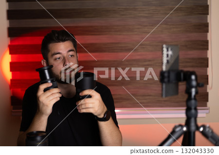 A man is demonstrating podcasting equipment, holding two microphones 132043330